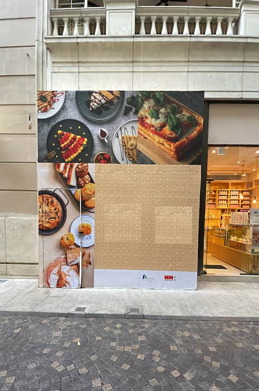 Ref#3022: Restaurant space for rent—storefront under renovation with a covered entrance featuring large food photos. Bright, modern interior visible on the right side. Ideal location for your dining business.