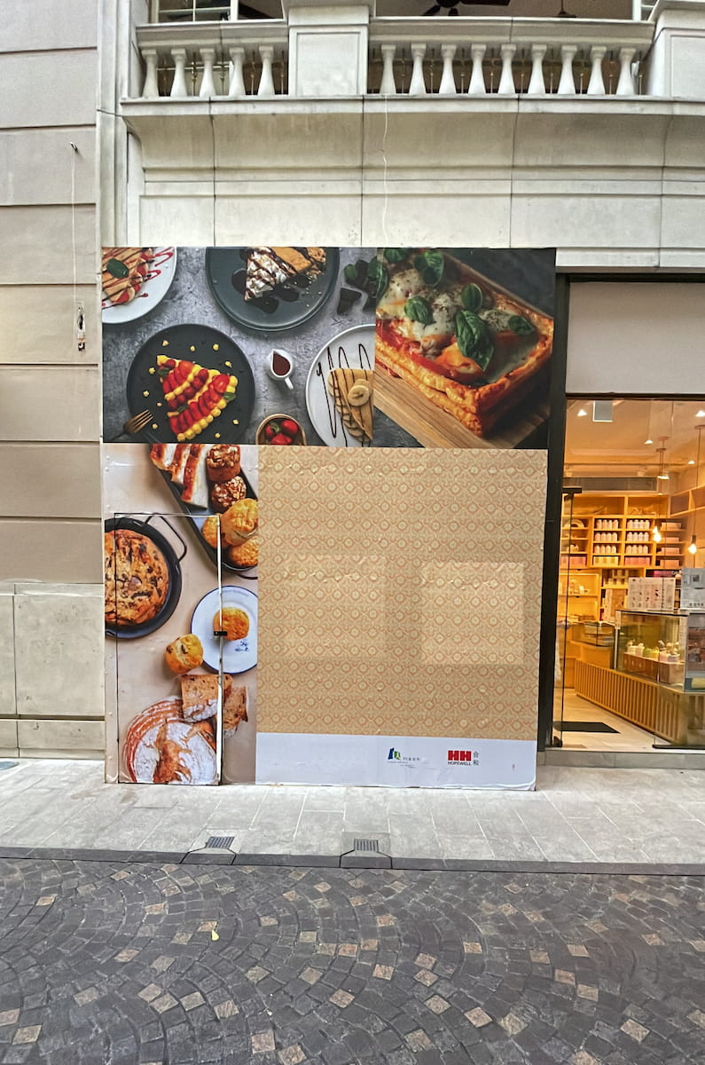 Ref#3022 is a storefront ideal for renting as a shop or restaurant, with large food photos on the exterior and part of the store covered in patterned paper. Next door, shelves display assorted packaged goods.