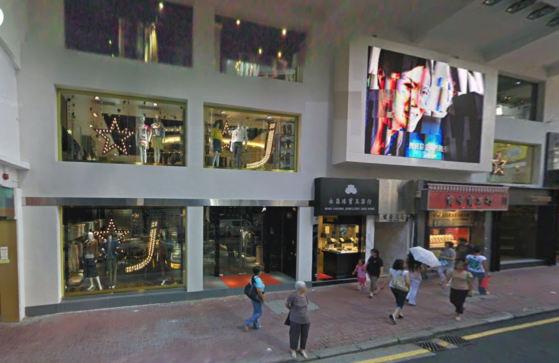 A city street features Ref#3030: people walk past brightly lit storefronts with mannequins, a large digital billboard showing a persons face, and prominent shop rental and office rental signs above the shops.