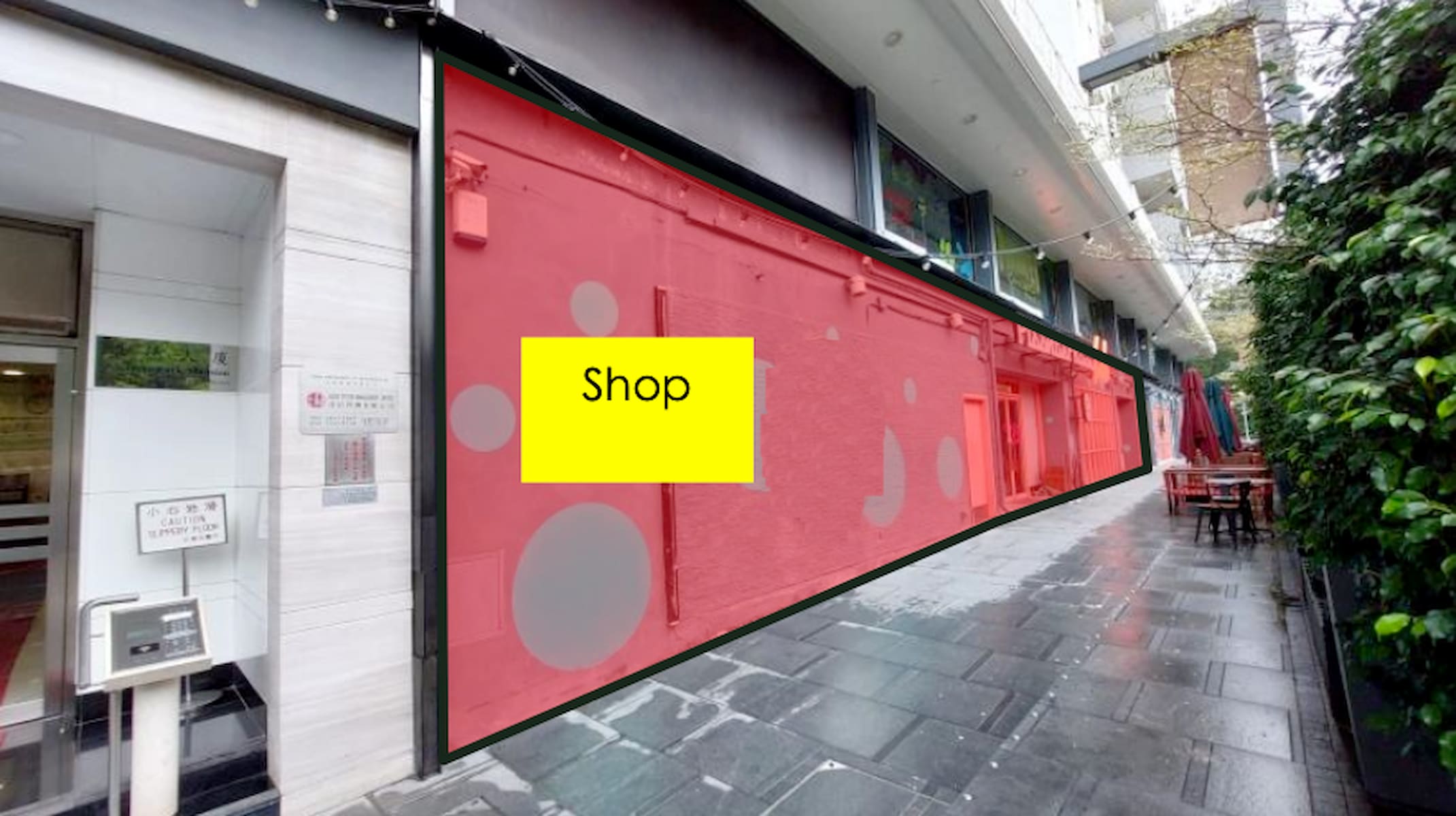 Ref#3028 is a shop with a red-painted exterior and bold yellow Shop sign, ideal for renting. It's located along a covered walkway with outdoor tables and greenery on the right.