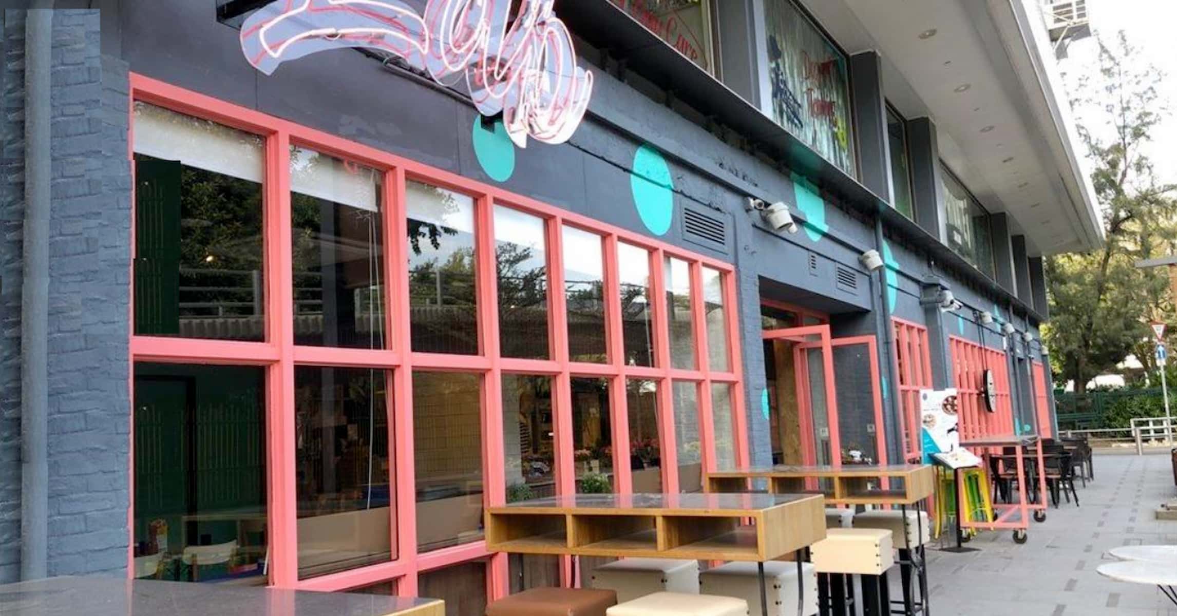 Ref#3028 features colorful tables and stools outside a modern café with pink-framed windows and turquoise accents—an inviting spot to rent a shop or restaurant, enhanced by tree-lined sidewalks.