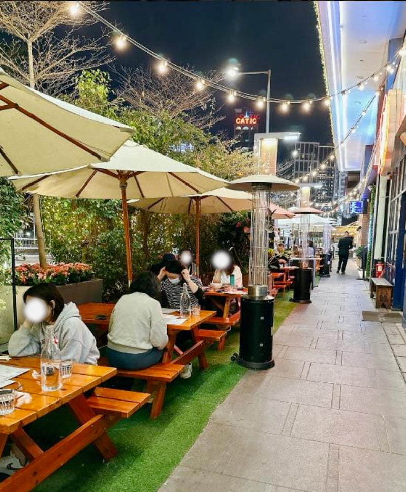 Ref#3029 creates an inviting nighttime restaurant scene with people dining at wooden picnic tables under large umbrellas, string lights above, and patio heaters between tables
ideal for a stylish city-sidewalk restaurant rental.