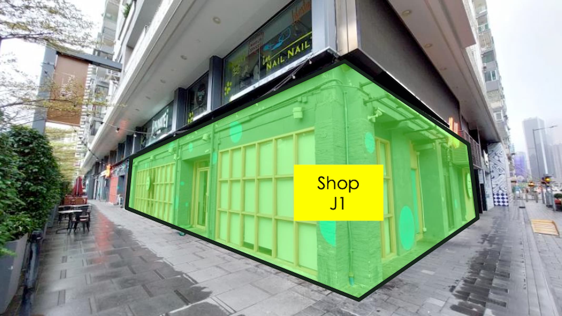 Ref#3029: A corner shop with green panels and a Shop J1 sign, situated on a city street amid tall buildings and wet pavement
 perfect for anyone seeking to rent shop space in a lively urban area.