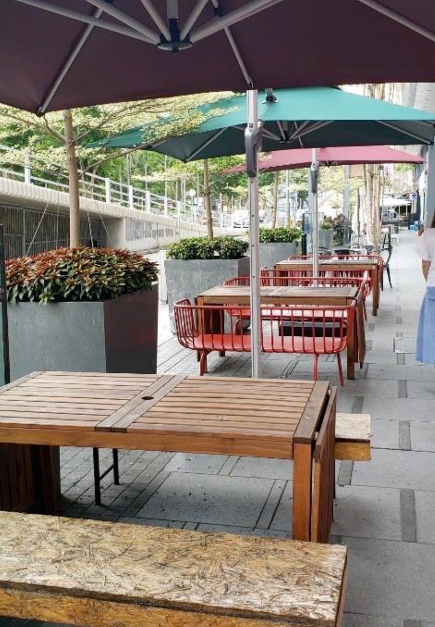 Ref#3029 features an outdoor seating area with wooden tables, benches, red chairs, potted plants, and green and purple umbrellas on a paved sidewalk
ideal for those seeking to rent nearby shop or office space.