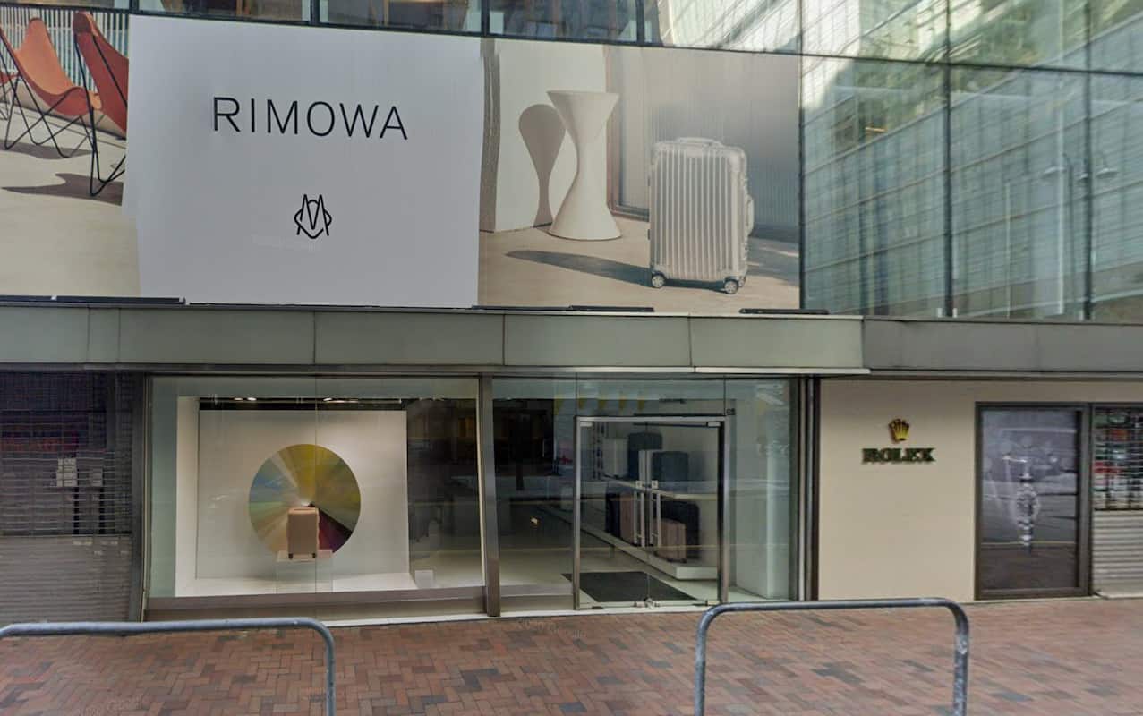 Street view of storefront Ref#3016 with a large RIMOWA luggage ad above glass windows, circular art display, and a nearby Rolex signideal for those seeking prime shop rental opportunities.
