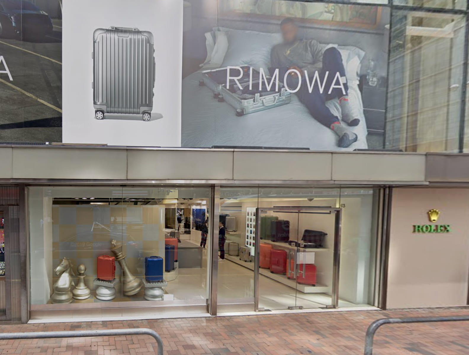 Storefront displays large RIMOWA luggage ads above, while a window showcases suitcases inside. The Rolex logo appears on the buildings right side, highlighting premium rental opportunities for Ref#3016. Street and sidewalk are seen in front.