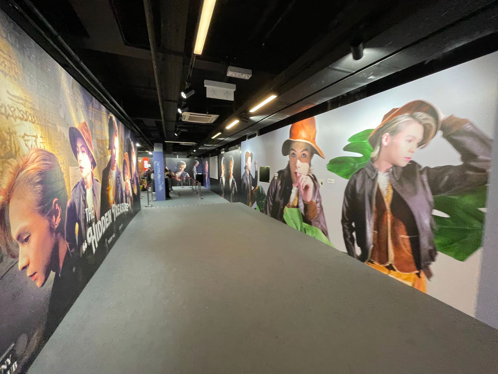 Ref#3015: A well-lit hallway with colorful murals featuring large portraits of stylishly dressed people, some in hats. Ideal for renting office or shop spaces; a few people are visible in the distance.