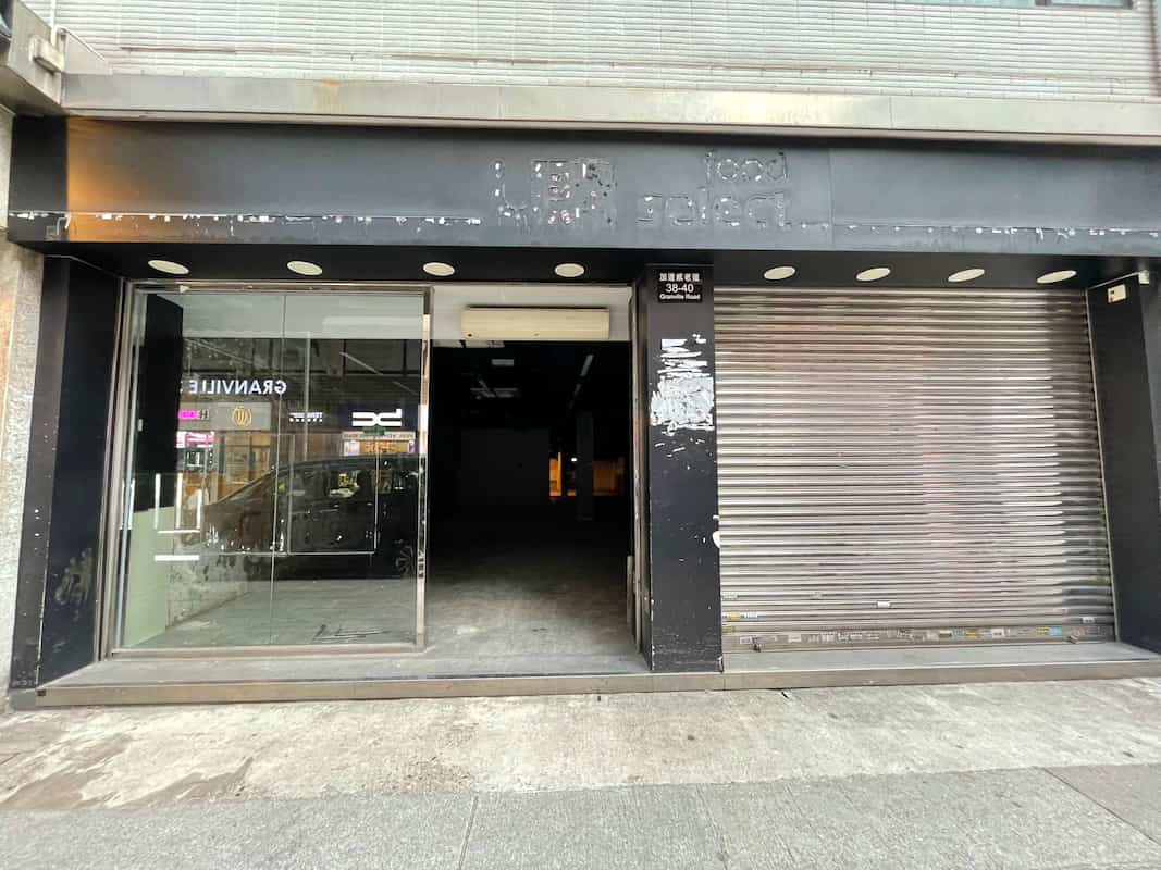 Ref#3015: Vacant storefront for restaurant rental with a glass door (left), closed metal shutter (right), and a faded sign above. A clean, worn sidewalk highlights the prime potential of this historic location.