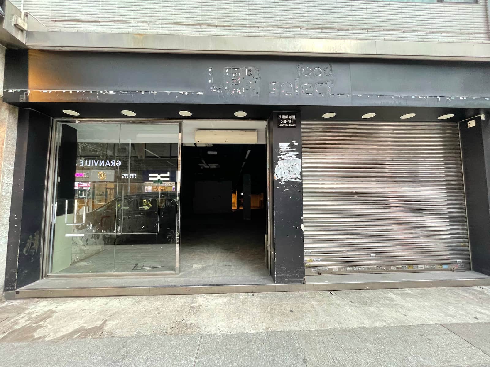 Ref#3015: Storefront for rent with a partially open glass door (left), closed metal shutter (right), dark empty interior, and faded signage above the entrance.