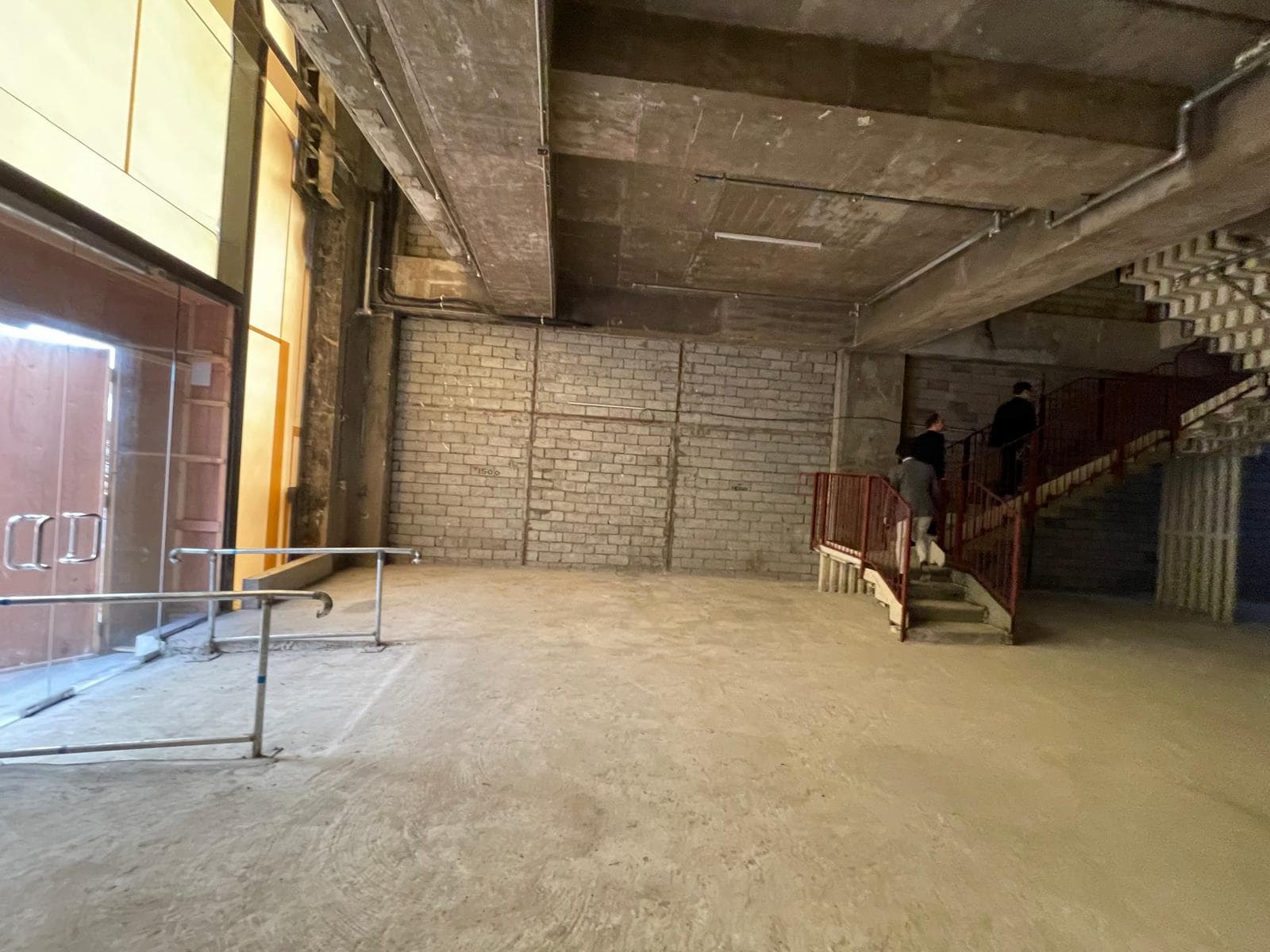 Ref#3014: Spacious unfinished interior with concrete floors, brick walls, and exposed ceilings
dual for a shop or office. Features include a red metal staircase on the right and a glass door with metal railings on the left.