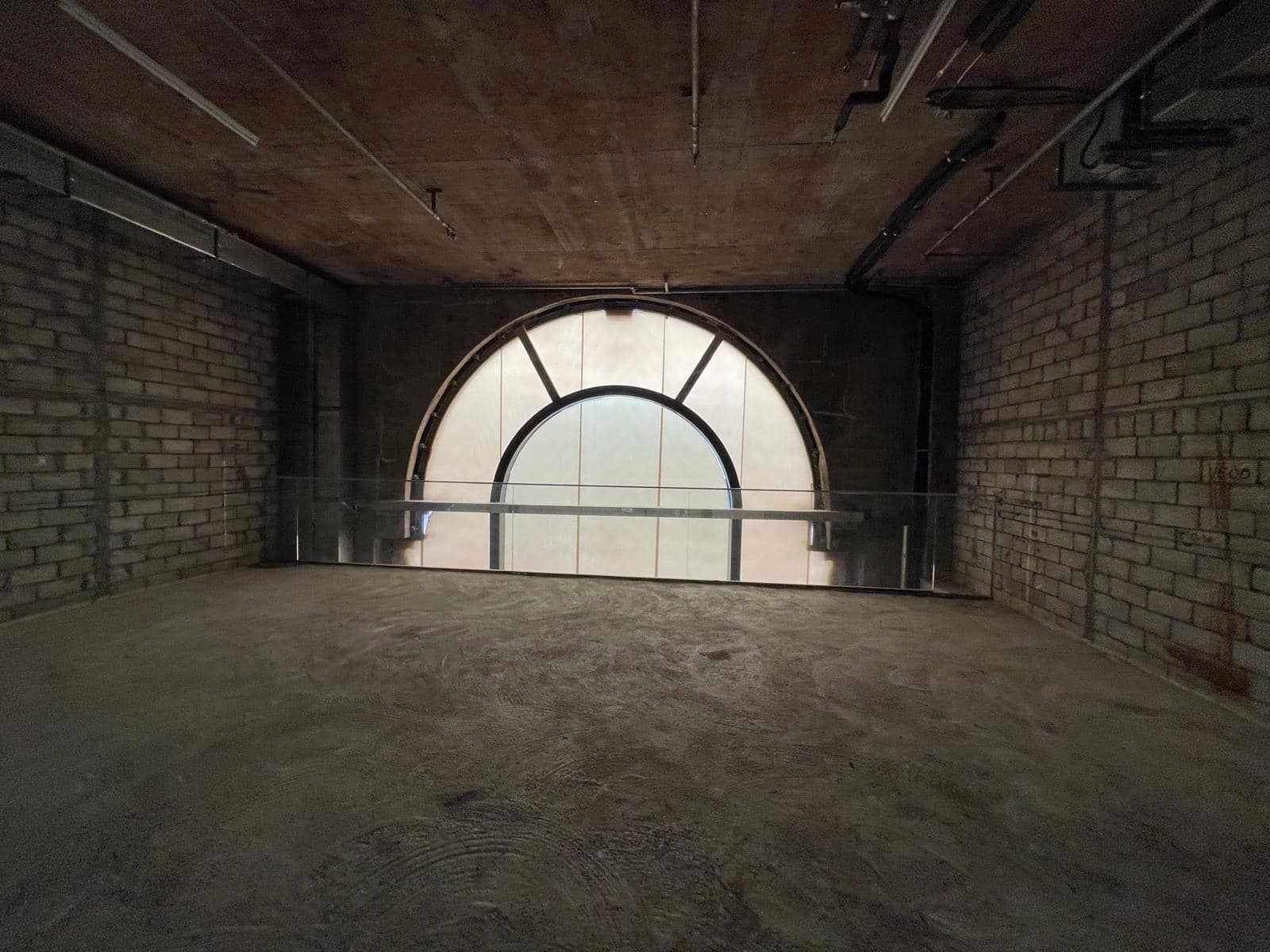 Ref#3014 is a dimly lit, unfinished space with concrete floors, brick walls, and a large arched windowperfect for renting as a restaurant or office with unique character and natural light.