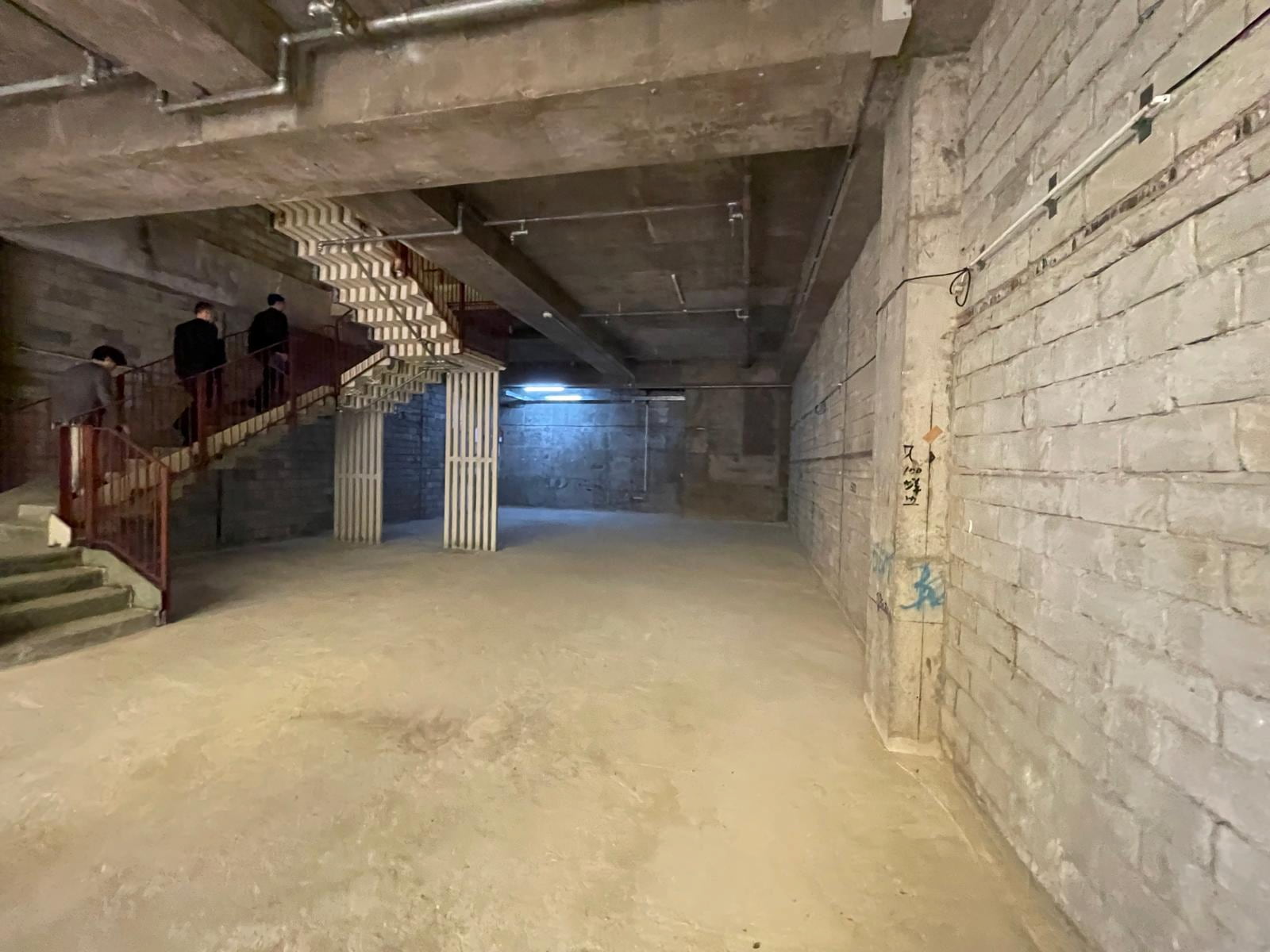 Ref#3014: Spacious unfinished basement with concrete floors and wallsperfect for office or shop rental. Features staircase access, fluorescent lighting, exposed pipes, and graffiti on the back wall.