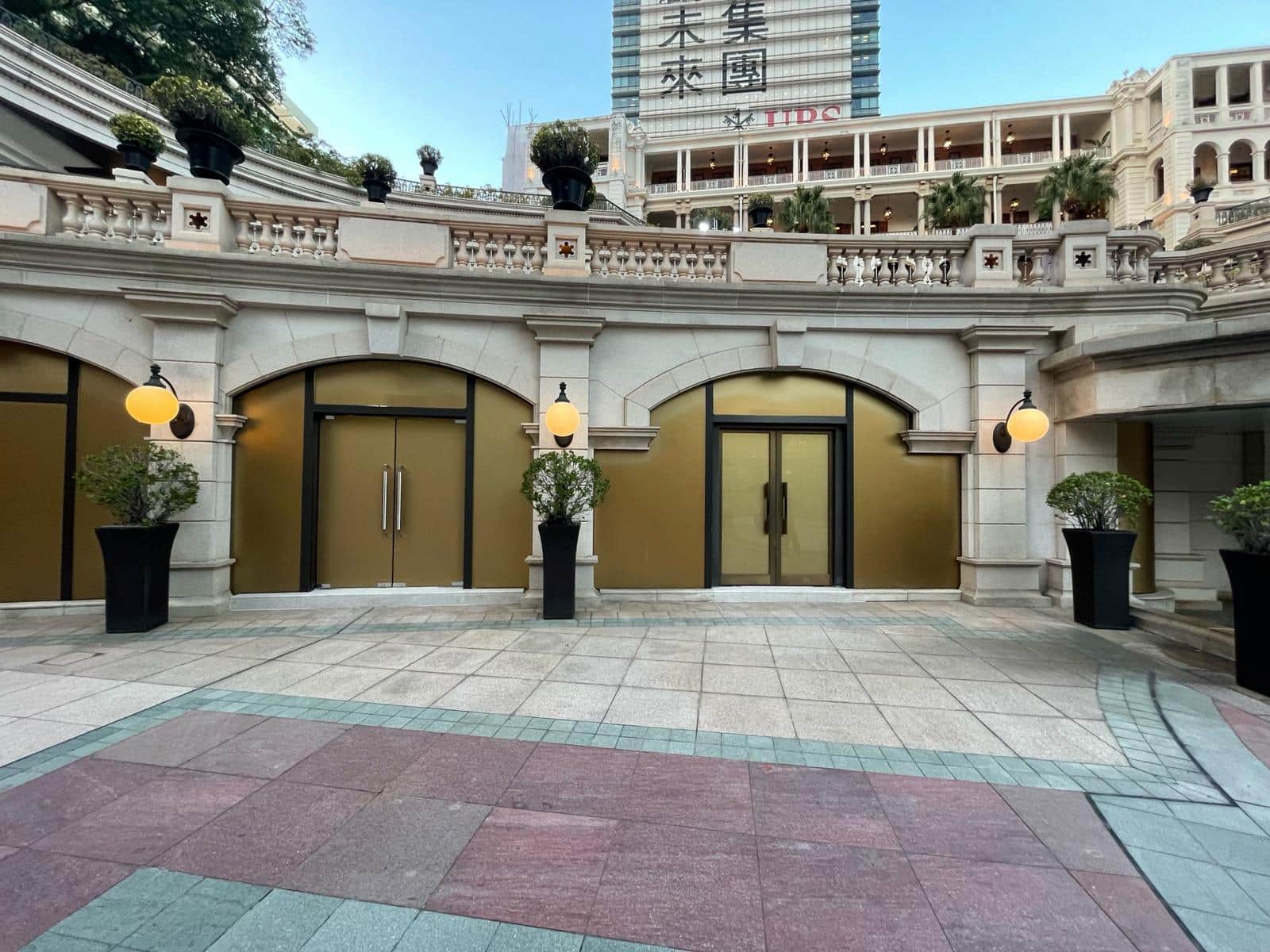 Ref#3012 features a courtyard with gold-paneled arched doorways, black potted plants, and globe wall lightsperfect for shop or office rentalset in a stone building with decorative railing and city high-rises beyond.