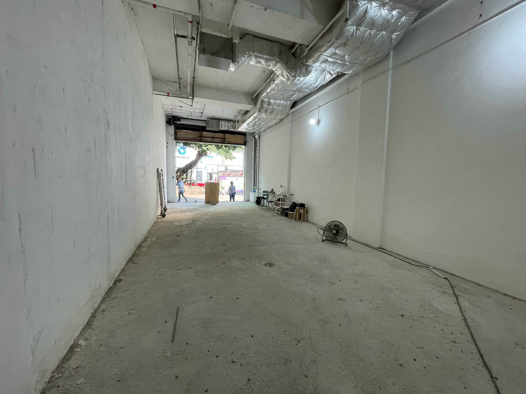 Ref#3009: Spacious, empty industrial room with high ceilings, exposed ducts, and concrete floorideal to rent as office or shop. Features large open doorway to the street, standing fan, and scattered items near entrance.