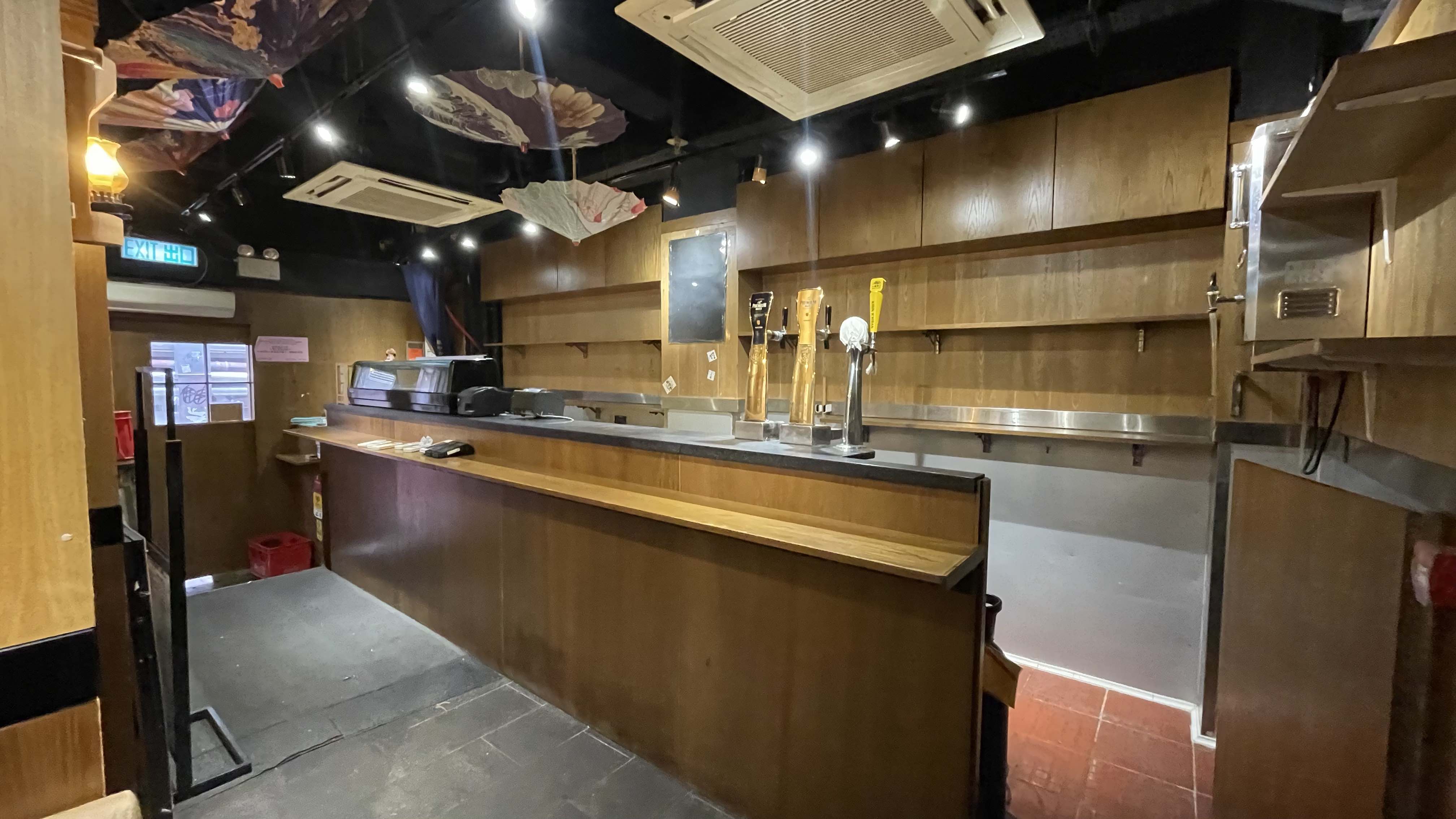 Ref#2995: An unoccupied bar with wooden counters, beer taps, wall shelves, ceiling lights, chalkboard, and equipment
perfect for restaurant or shop rental.