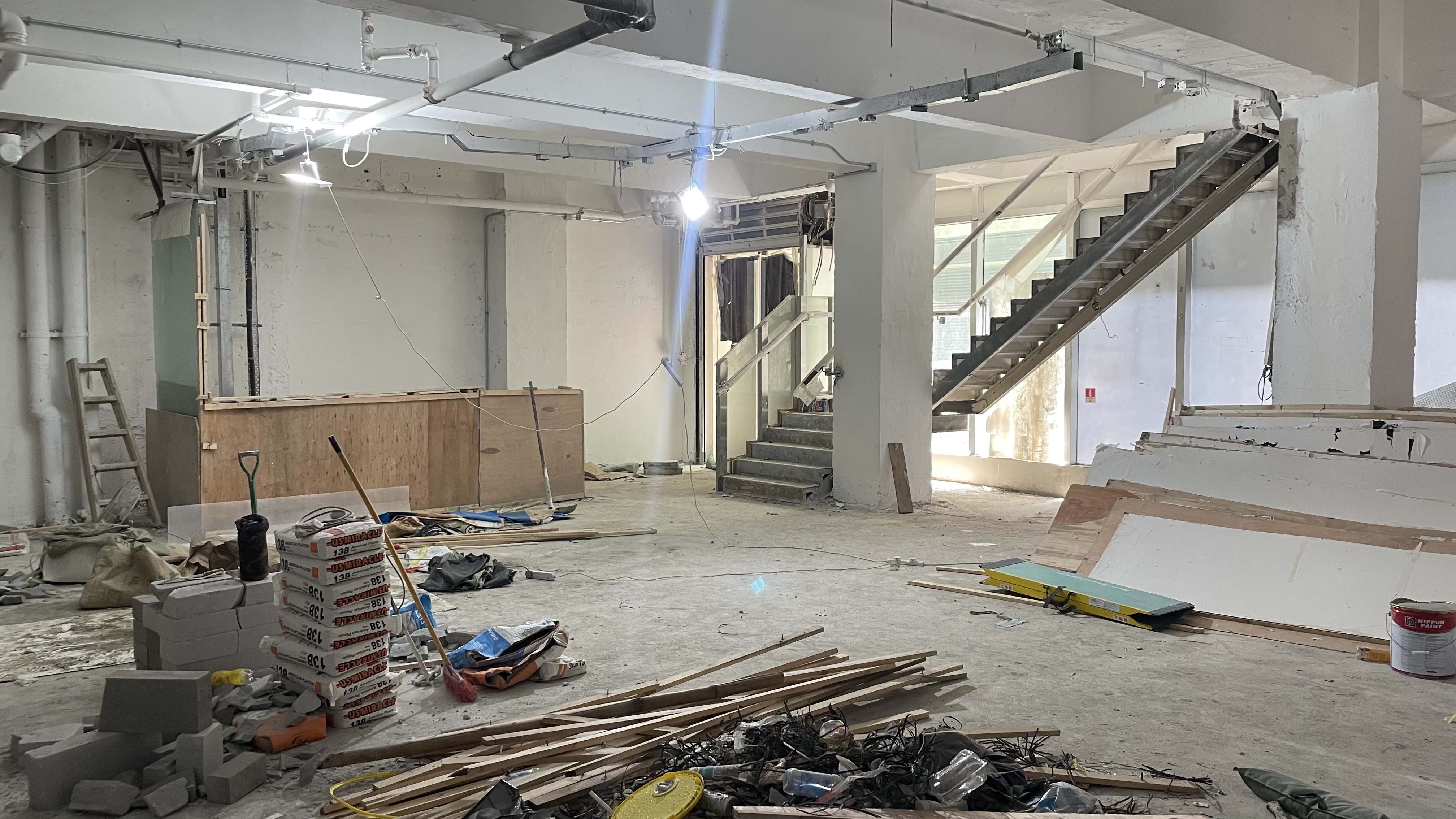 Ref#2987: Large unfinished indoor space under renovation, ideal for shop or office rental. Features construction materials and debris, exposed wiring and pipes, plus an incomplete staircase to the upper level.