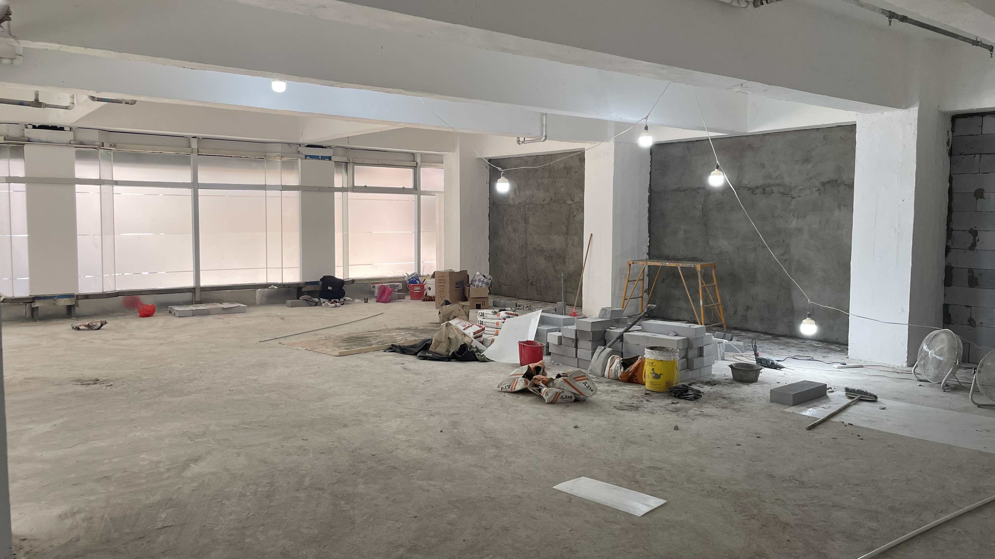 Ref#2987: A spacious, unfinished room with exposed concrete walls, construction materials, cinder blocks, buckets, ladder, and hanging bulbs94perfect to rent for your next restaurant or shop.