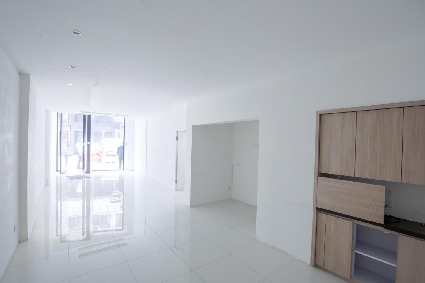 Ref#2981 features a bright, empty room with white tiled floors, white walls, large front windows for natural light, and a wooden cabinet1 ideal for restaurant or shop rental.