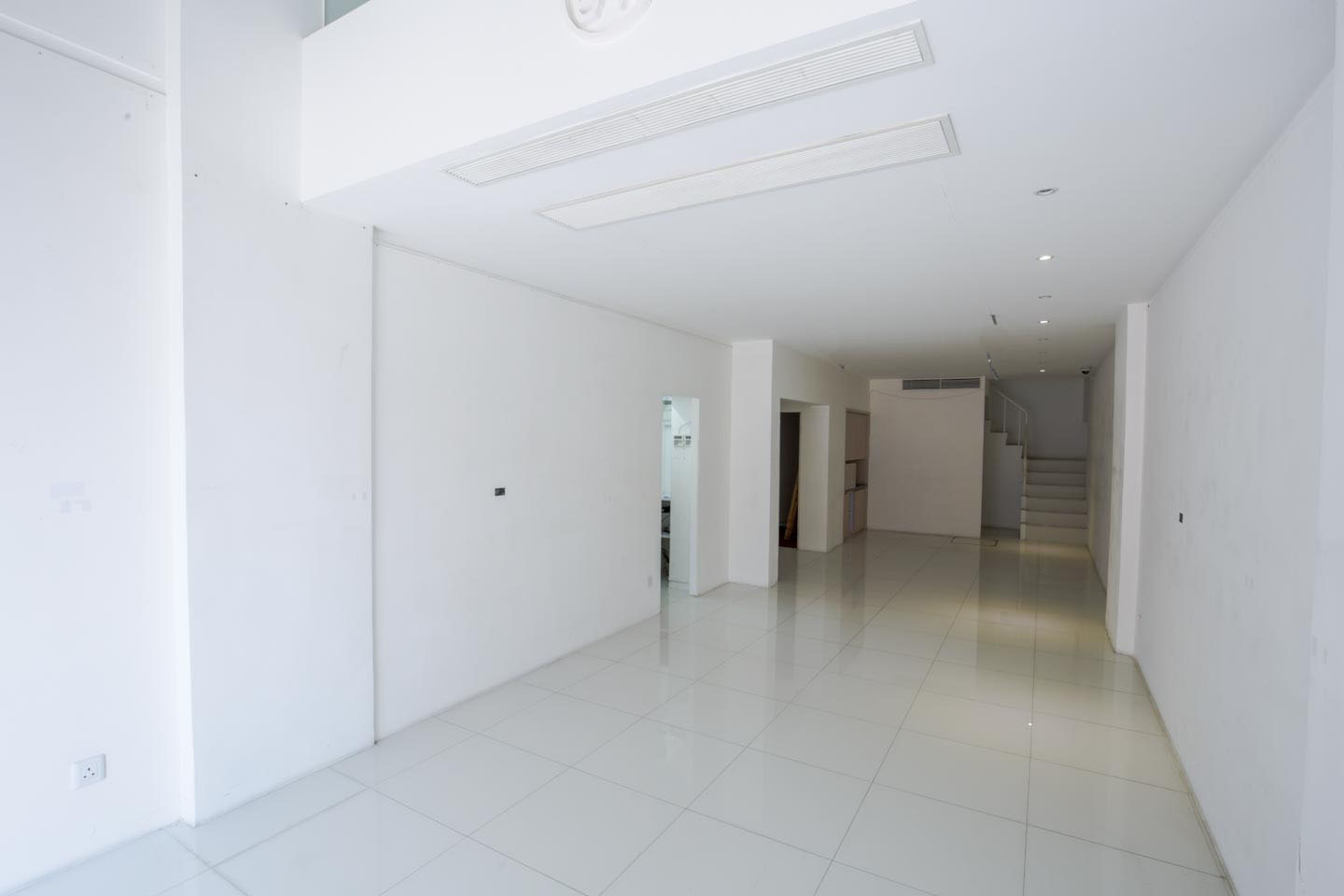 Ref#2981 offers a spacious, well-lit room with white walls, tiled floors, ceiling lights, and a rear staircase to an upper level1 ideal for minimalistic shop or office rental.