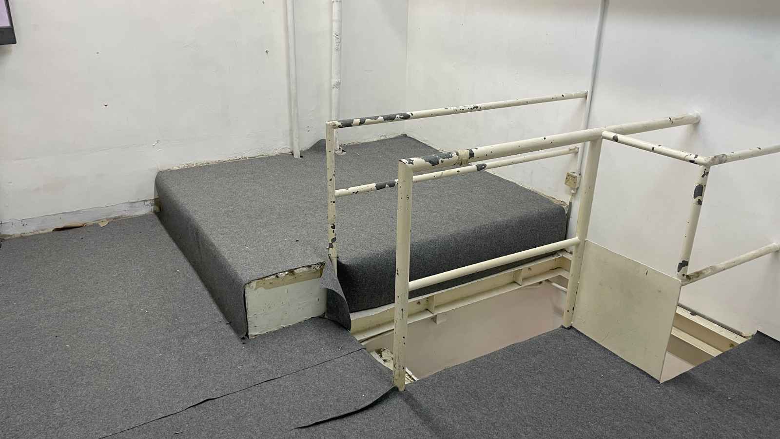 Ref#2982 features a gray-carpeted platform with peeling edges and chipped, white metal railings40an unfinished, worn space ideal for those looking to rent a shop or convert it into a unique restaurant or office.
