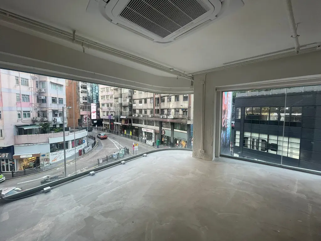 Ref#2980: Spacious empty room with concrete floors, floor-to-ceiling windows overlooking a vibrant city street. Ideal for office or shop rental; features ceiling air conditioning for comfort.