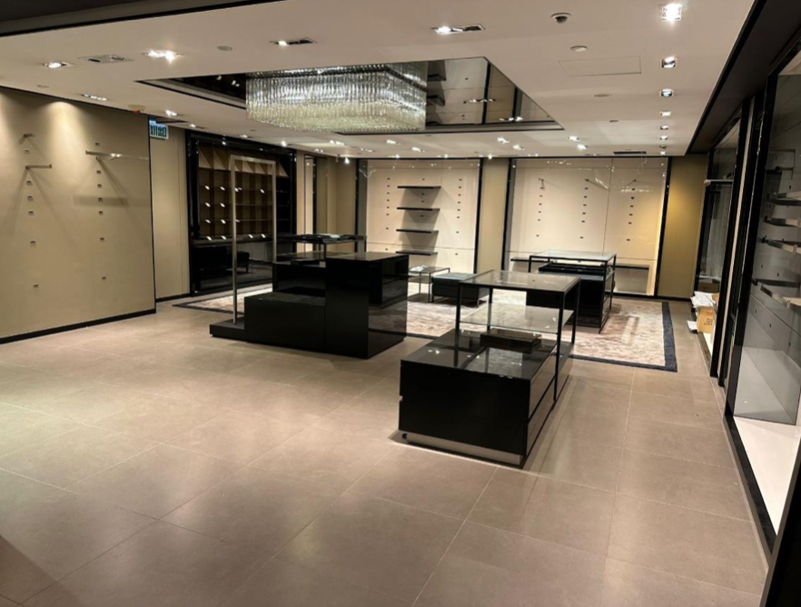 Ref#3120: Spacious, modern retail shop for rent with beige walls, glass display cases, black shelves, and a large chandeliermove-in ready for your merchandise and customers.