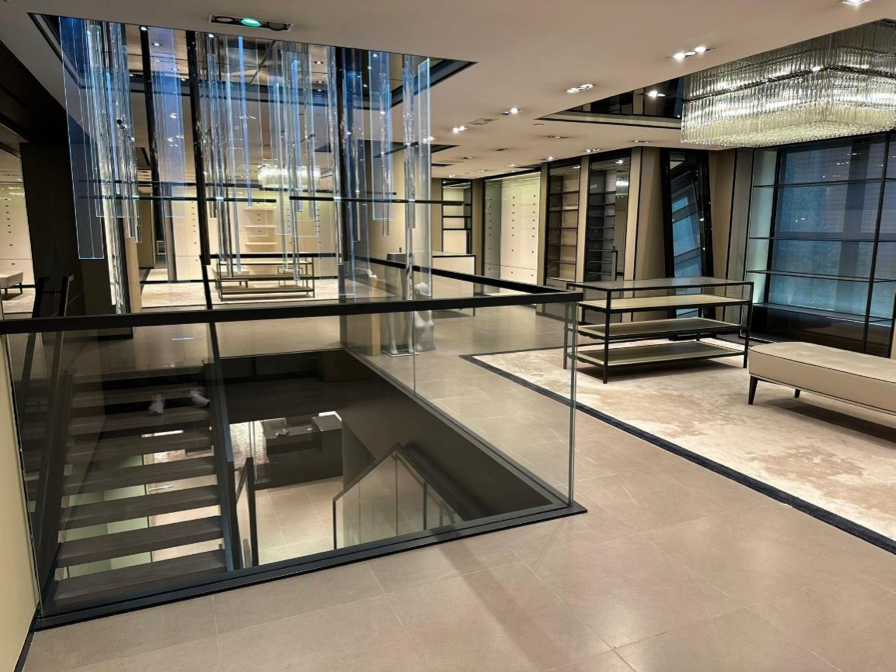 Ref#3120 offers a modern, spacious interior for office or shop rental, featuring glass railings, open staircase, sleek shelving, large windows, hanging light fixtures, neutral tones, and minimalist design.
