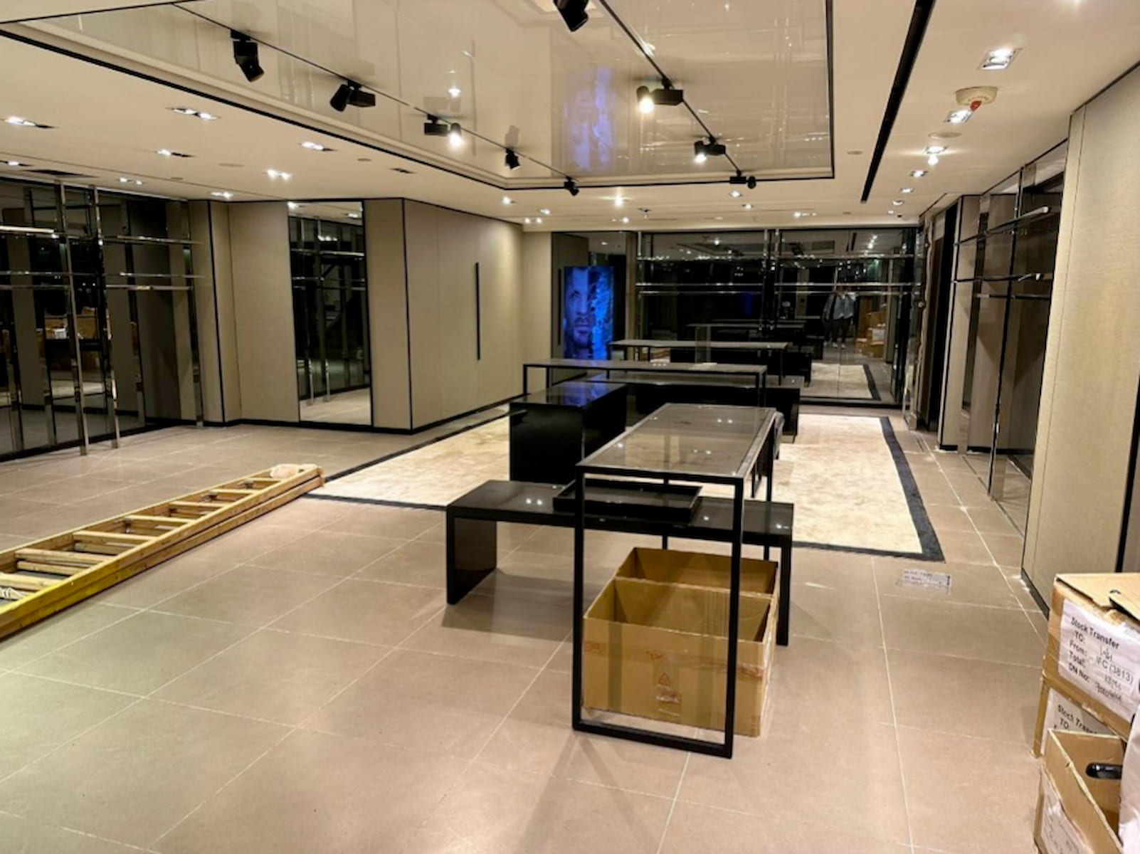 Ref#3120: A modern, empty retail store interior with glass display tables, wall mirrors, overhead lights, a ladder, and scattered boxesperfect for shop or office rental during setup stages.