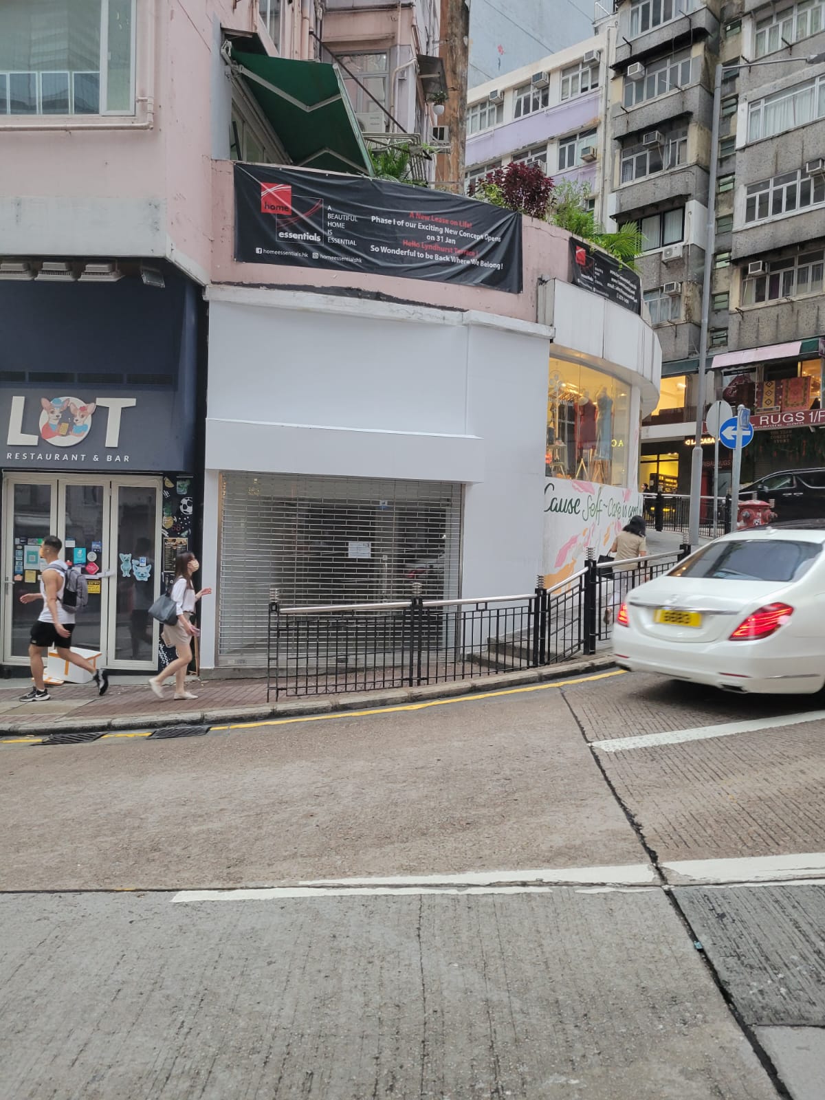A street scene shows pedestrians passing by Ref#2988, a restaurant rental, and a closed white-front shop. A white car drives along the sloped road, with tall buildings visible in the background.