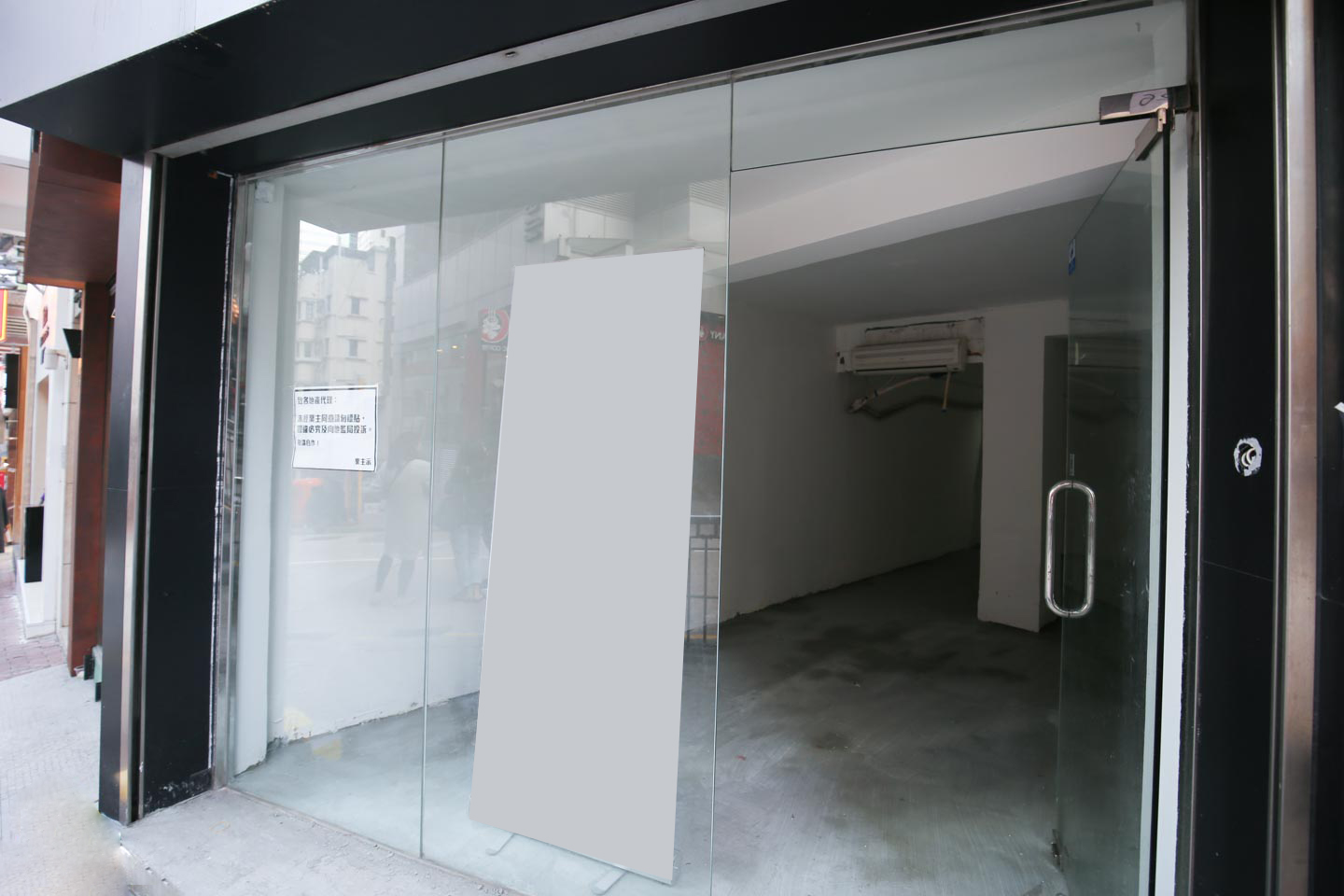 Ref#2988: Vacant storefront with glass doors and windows, empty interior, and a large blank sign at the front—perfect for shop rental. Reflections of buildings and people appear on the glass.