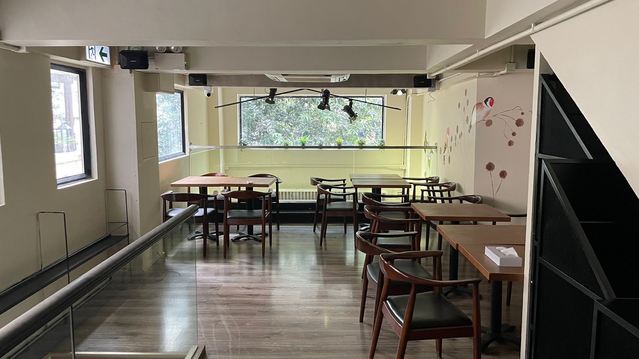 Ref#2994 is a bright, empty café with wooden tables and chairs, large windows for natural light, and potted plants on the windowsill—an inviting space to rent as a shop or restaurant.