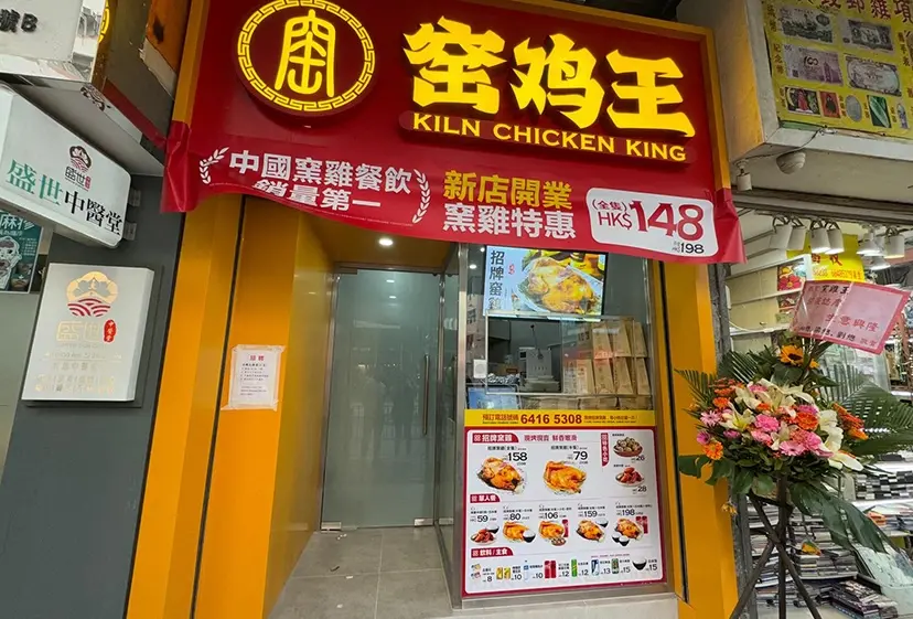 Shop on Shau Kei Wan Road, Shau Kei Wan. Restaurant entrance with Kiln Chicken King sign in red and yellow, menu display, and flower stand.