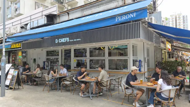 Restaurant space on Fung Yau Street South, Yuen Long. People dine at outdoor tables under a blue awning, at a casual restaurant.
