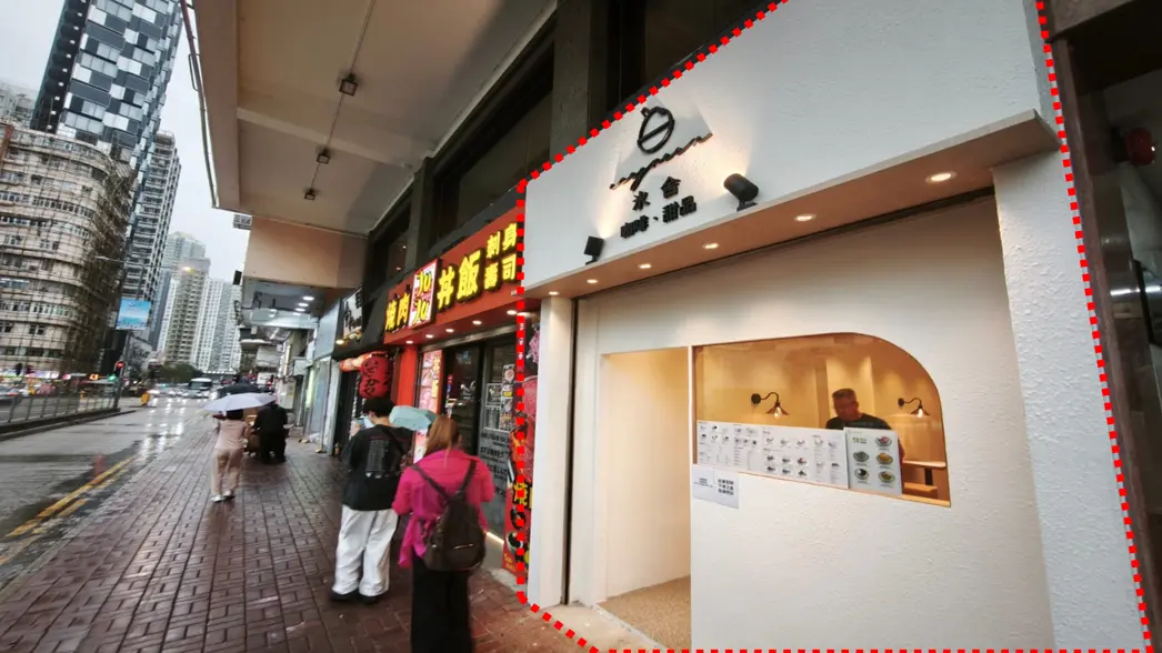 Shop on Sai Yee Street, Mong Kok. People with umbrellas on a wet Sai Yee Street sidewalk near shops and a white storefront displaying a menu.