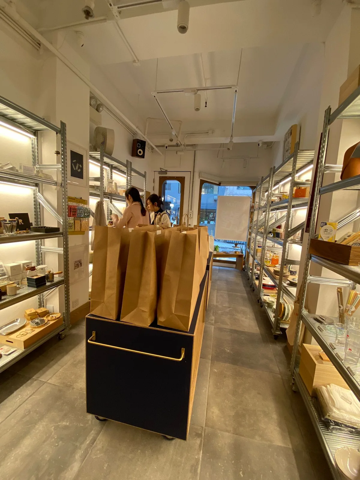 Two people behind a counter with paper bags in a modern Second Street store in Sai Ying Pun, shelves lined with goods.