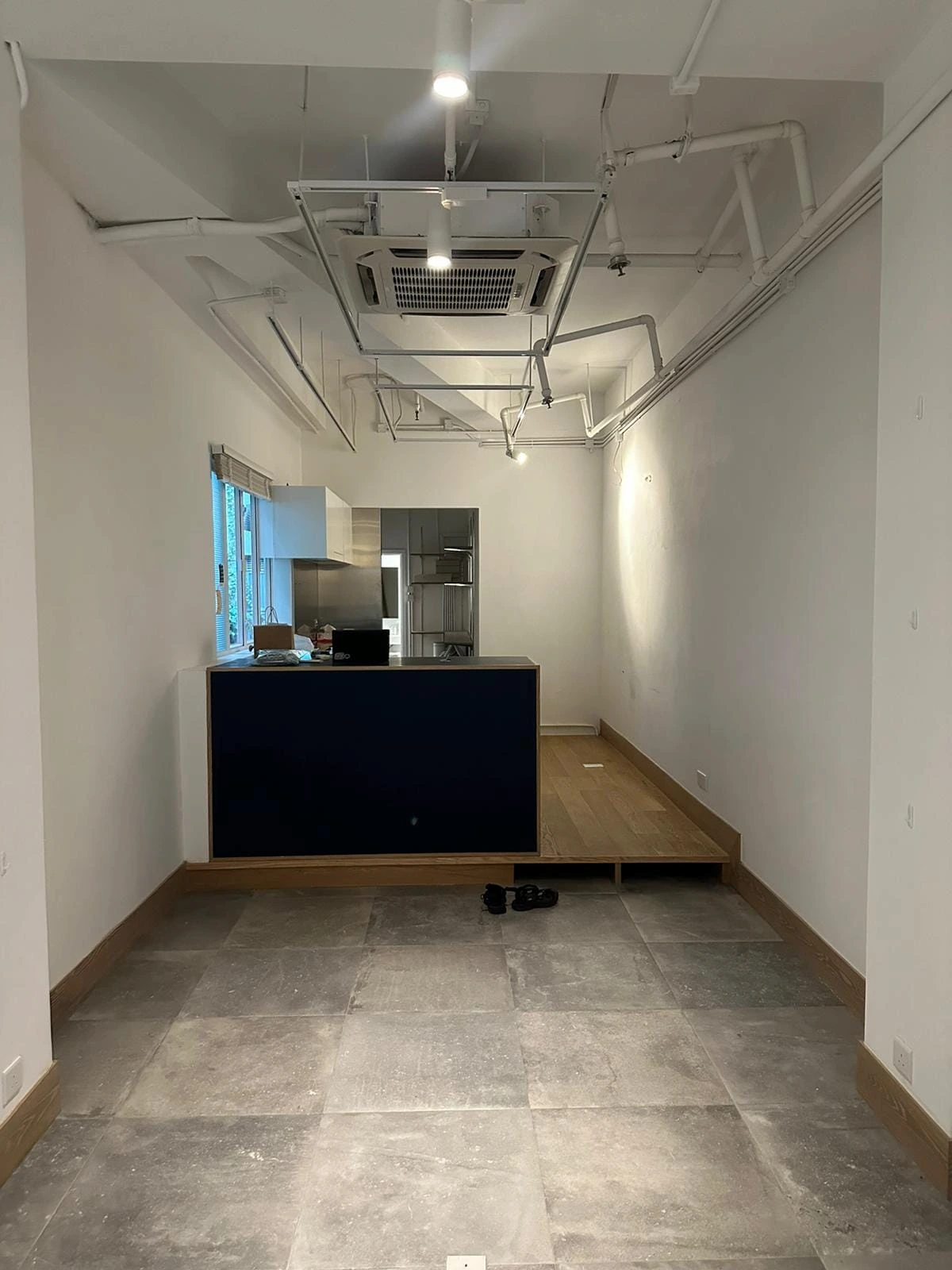 Mostly empty office on Second Street in Sai Ying Pun with a raised platform, exposed ceiling pipes, and shoes on the floor.
