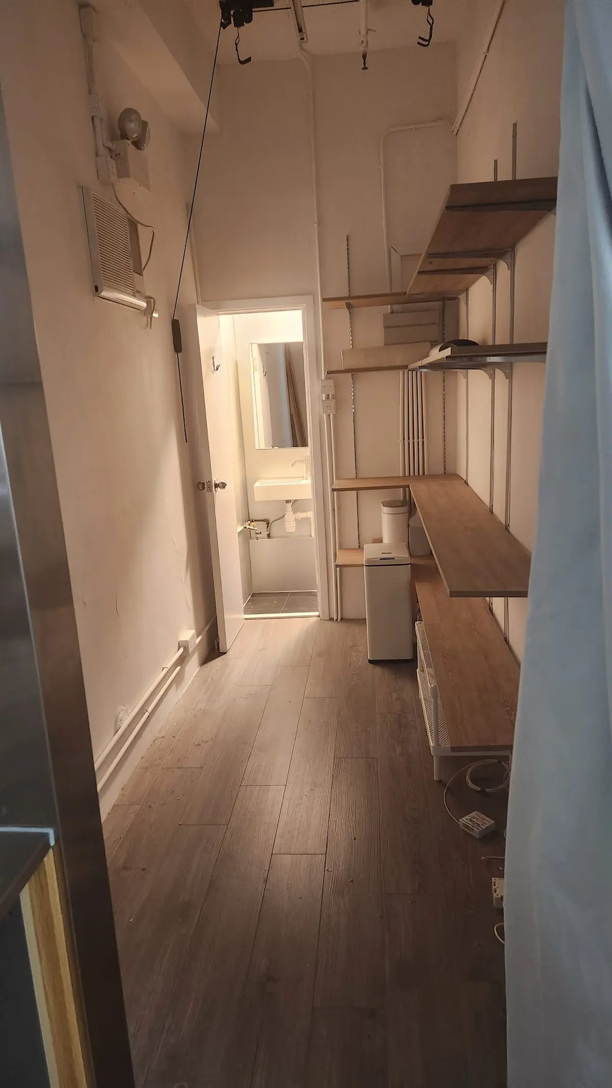 Narrow room on Second Street in Sai Ying Pun with wood floor, open shelves, small fridge and bathroom in view.