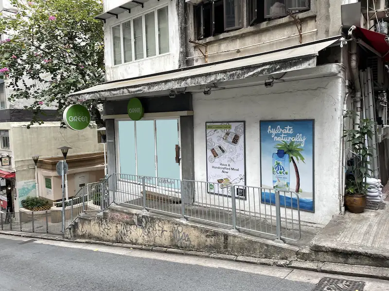 Shop on Graham Street, Central. Closed storefront on sloped Graham Street, Central, with posters and round green signs labeled “GREEN” above the entrance.