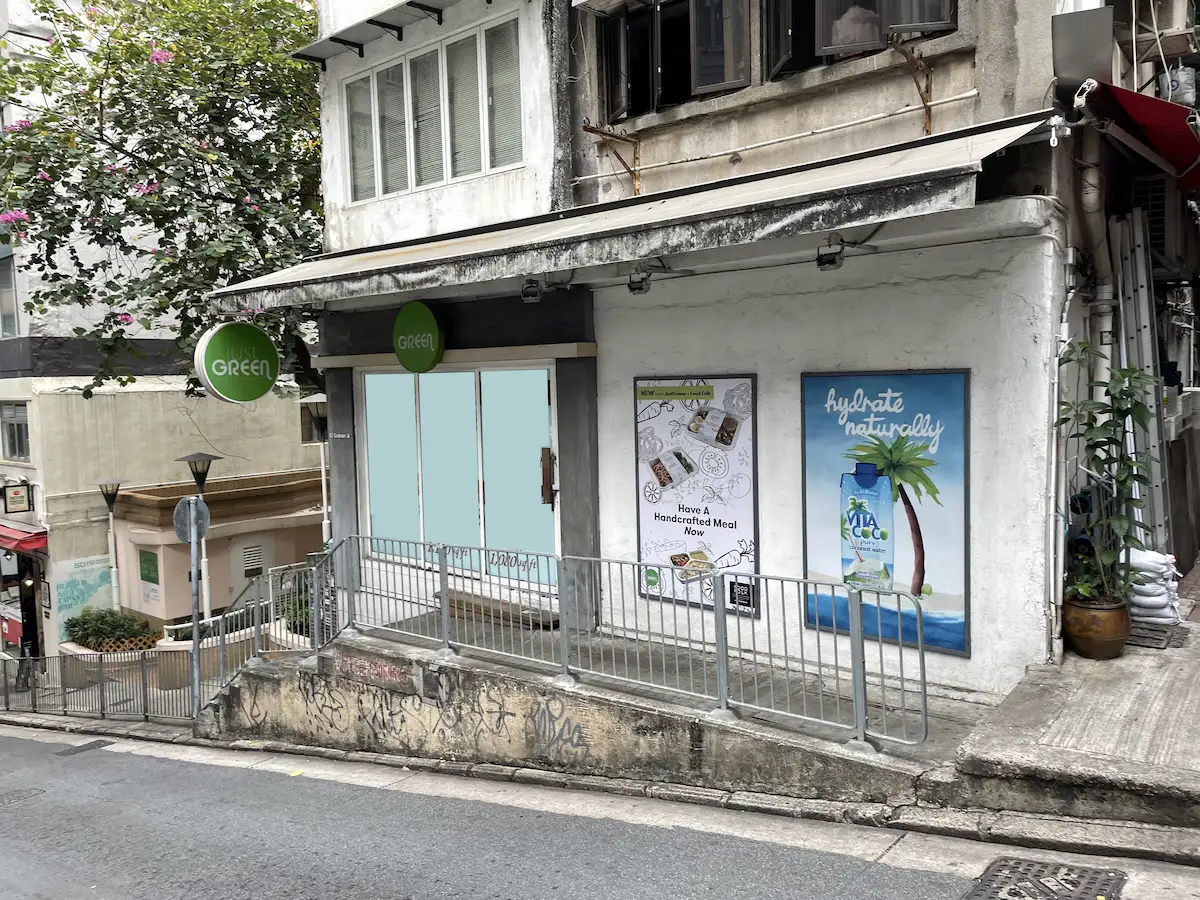 Small storefront on Graham Street in Central with exterior wall ads for meals and coconut water, located on a slope.