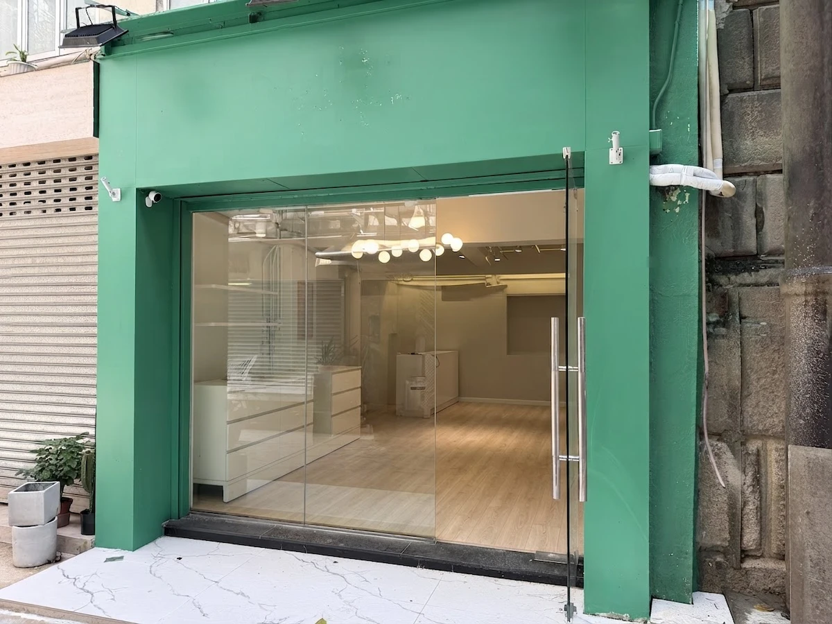 Small Sheung Wan storefront with green facade, glass door, light wood floors, and white walls.