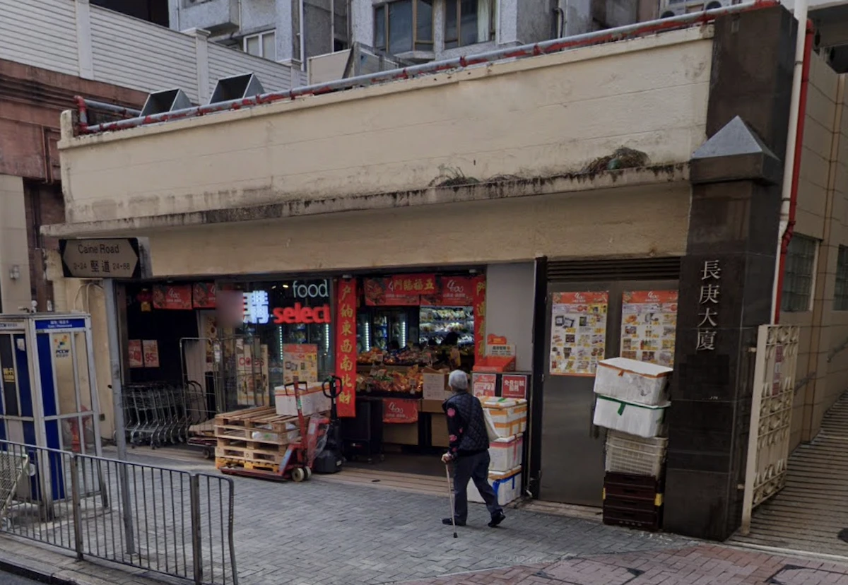 A person with a cane walks by a small grocery store with stacked boxes on Caine Road in Mid-Levels.