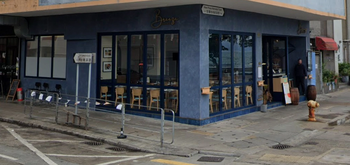 Blue corner café with large windows on New Praya, Kennedy Town, with a person waiting near the entrance on the street.