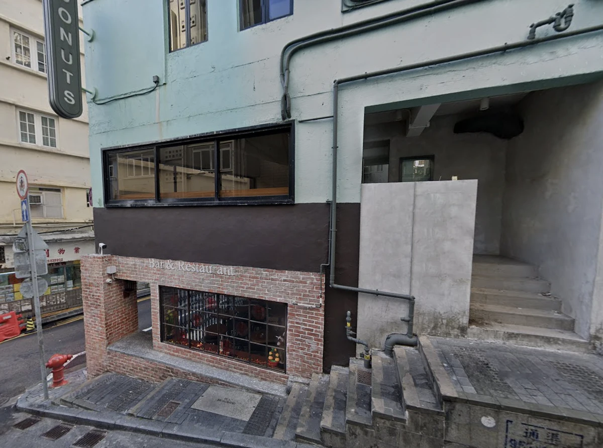 Brick restaurant entrance below street level on Elgin Street with stairs next to a gray building and large window above.