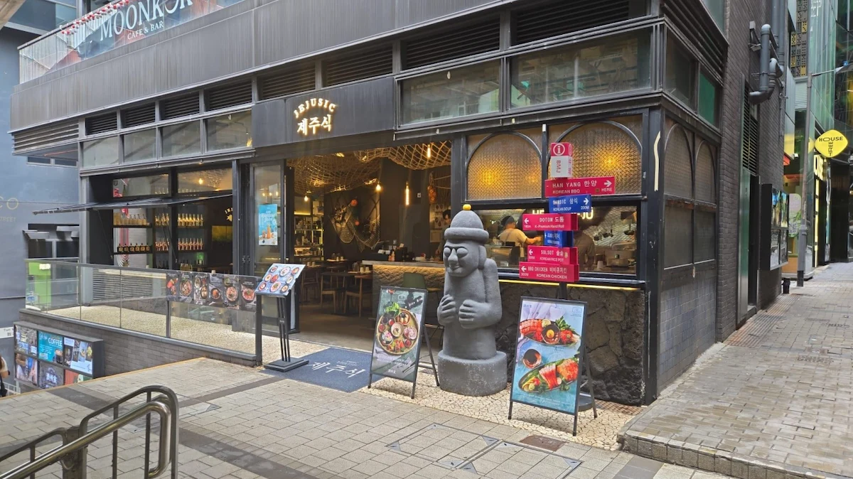 Restaurant with large windows, food signs, and a stone statue on Cochrane Street in Central.