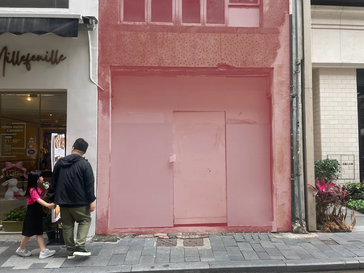 A man and a girl walk by a solid pink building facade on Staunton Street in Central Hong Kong.