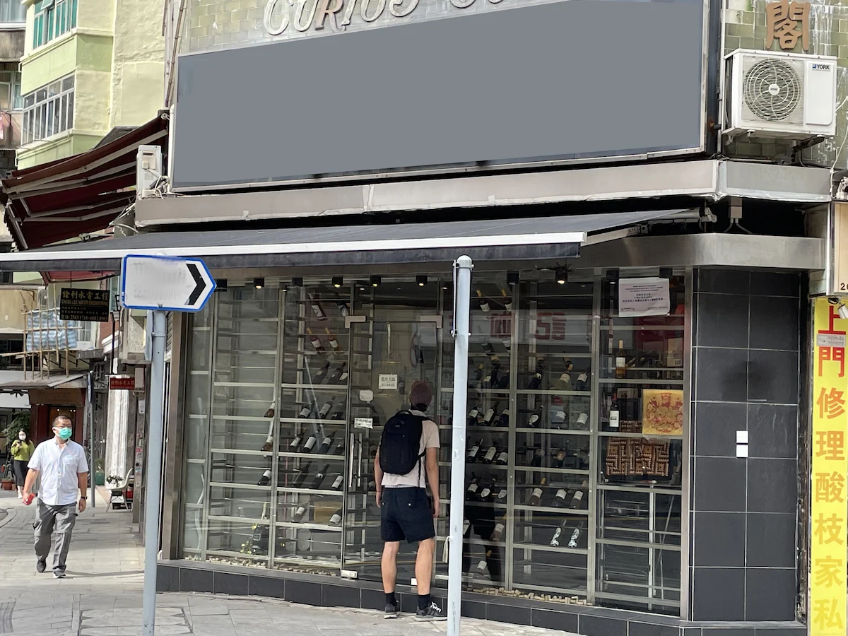 A man with a backpack looks into a shop window on Hollywood Road while another person walks by in Sheung Wan.