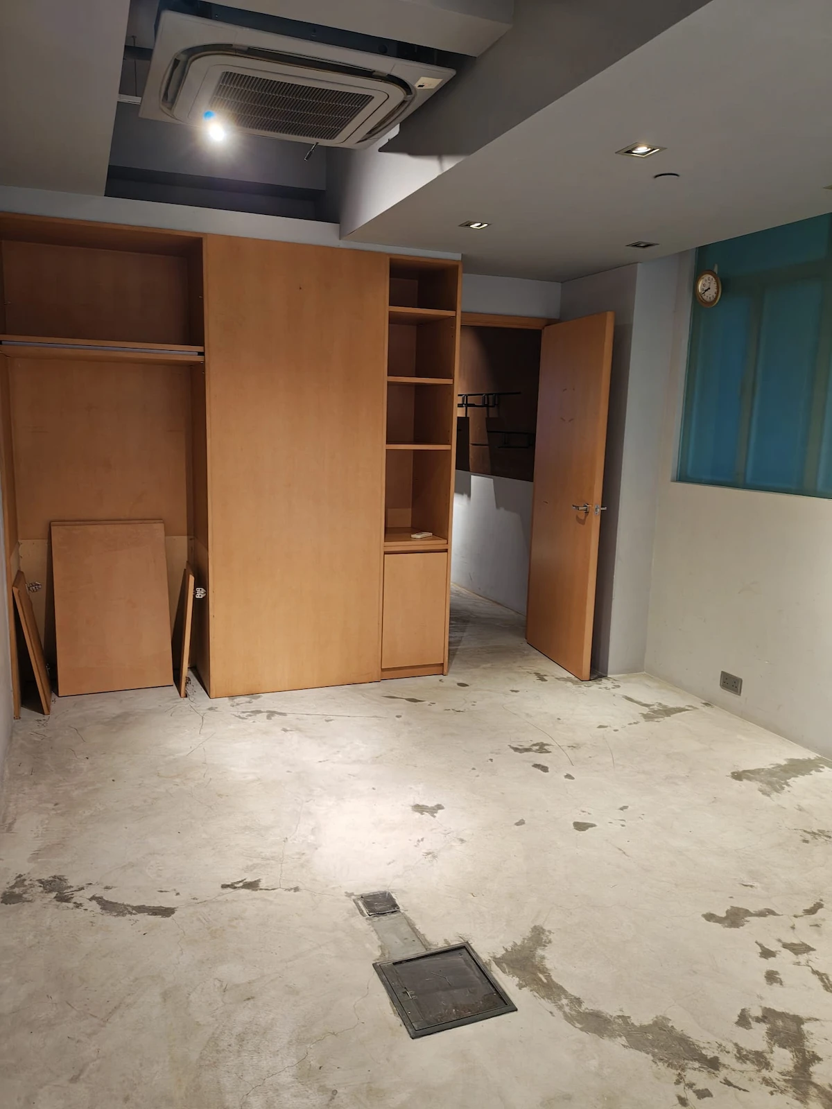 Empty room on Hollywood Road in Sheung Wan with built-in shelves, open closet, concrete floor, blue window, and AC.