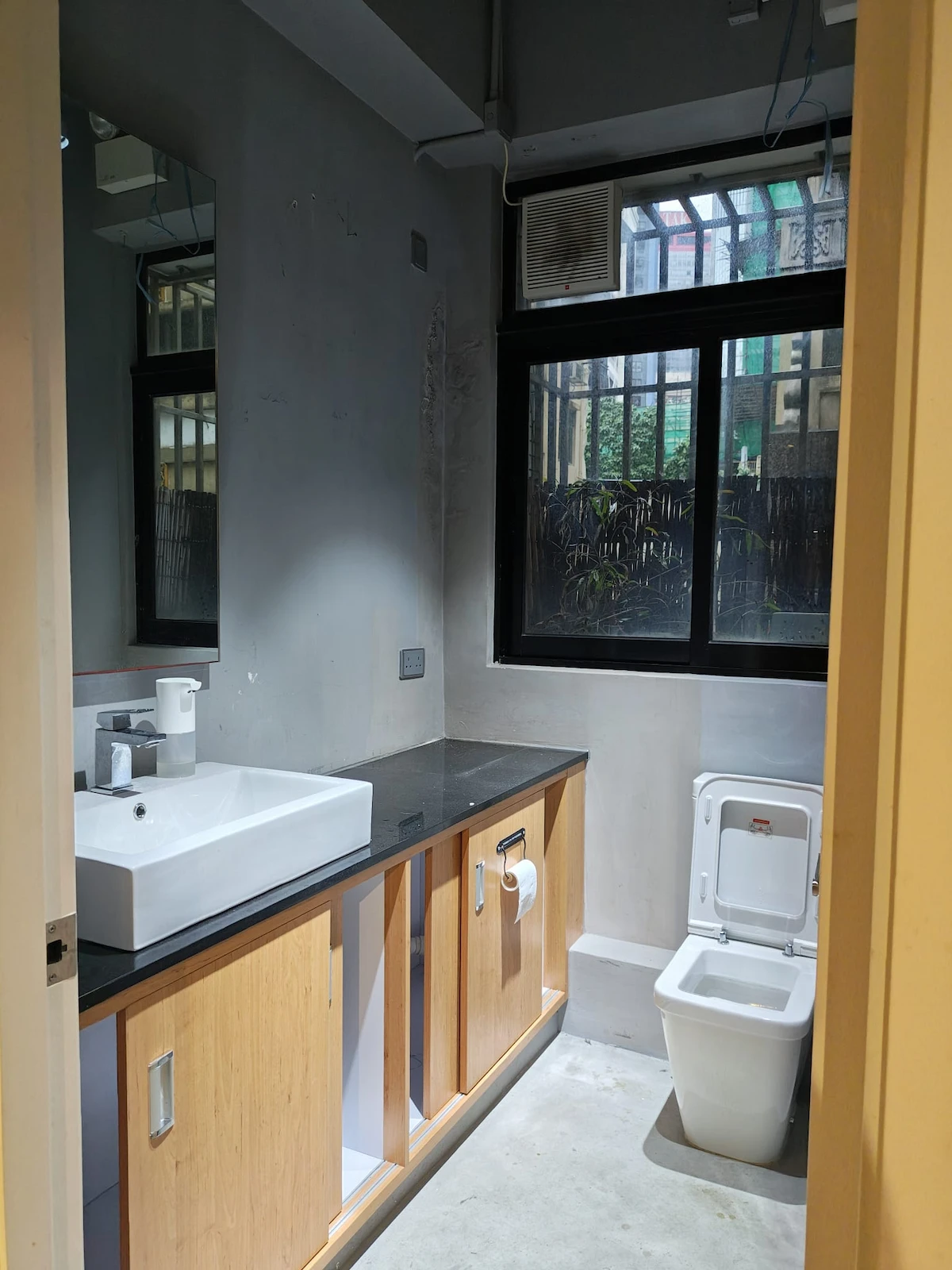Bathroom on Hollywood Road, Sheung Wan, featuring a sink, wooden cabinets, mirror, toilet and a large sunlit window.