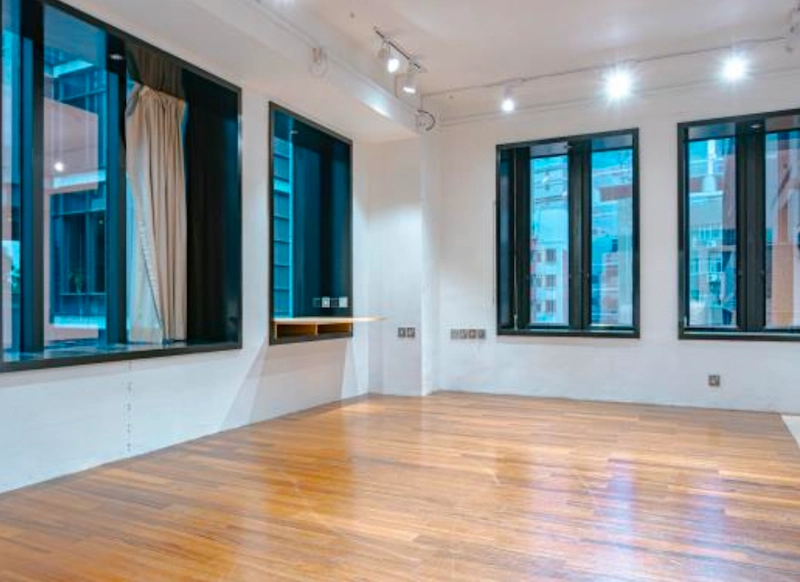 Shop on D'Aguilar Street, Central. Empty room on D’Aguilar Street with wooden floor, large windows, white walls, ceiling lights, and a beige curtain.