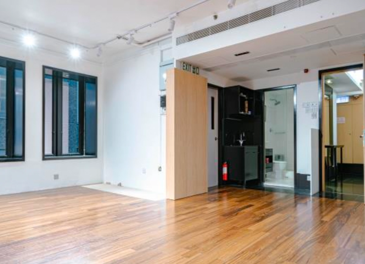 Empty room with wood floors on D’Aguilar Street, Central, large windows, kitchenette, and an open Exit door.